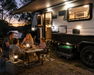 Caravan lights powered by 12V 200AH battery, with family sitting at a table outside by a lake at dusk.