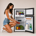 Woman reaching into a small refrigerator filled with food items.