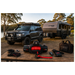 Black SUV with a trailer and outdoor equipment on a wooden table by a lake.