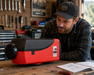 Man examining a red and black caravan diesel air heater in a workshop setting.