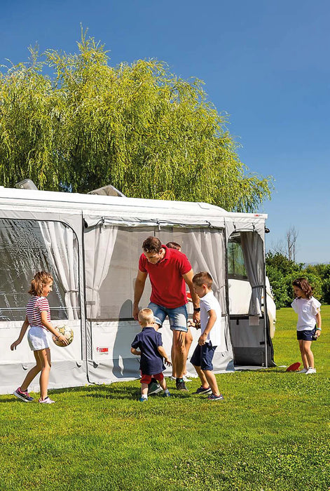 Family with children near a caravan with an awning on a sunny day.