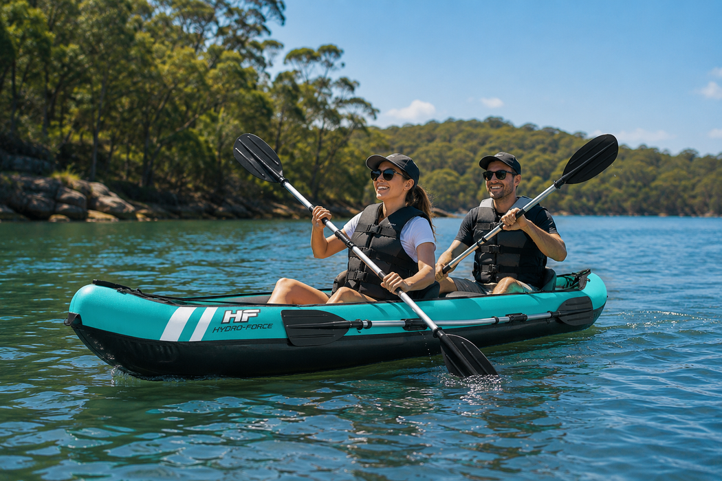Two people paddling a teal inflatable kayak on a calm lake with trees in the background.