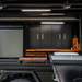 Storage compartment with black cabinets, wooden shelves, and a fridge/freezer inside a vehicle.