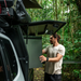 Man interacting with a vehicle-mounted refrigerator in a forest setting