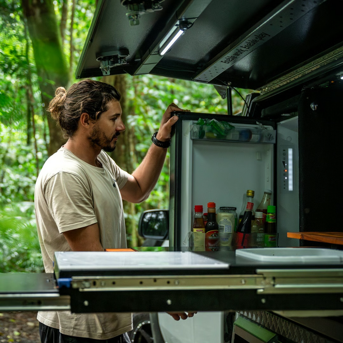 Man opening a refrigerator in an outdoor setting with greenery.