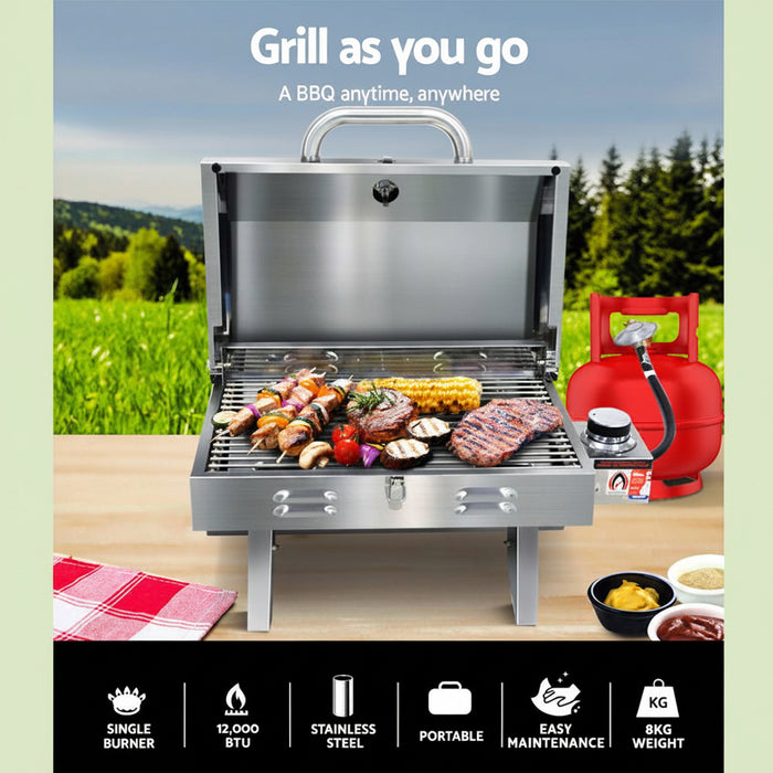 Portable BBQ with food on a table outdoors, surrounded by nature.