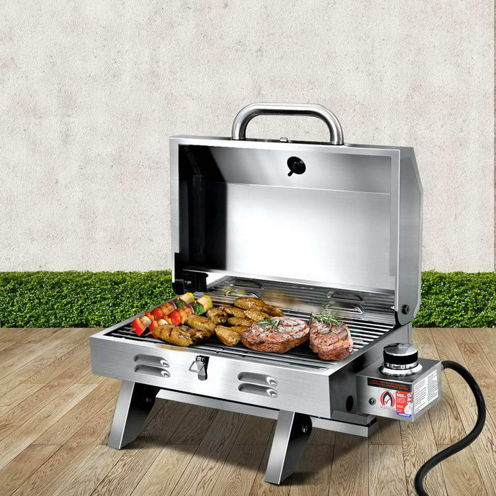 Portable gas BBQ with food on a wooden floor.