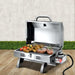 Portable gas BBQ with food on a wooden floor.