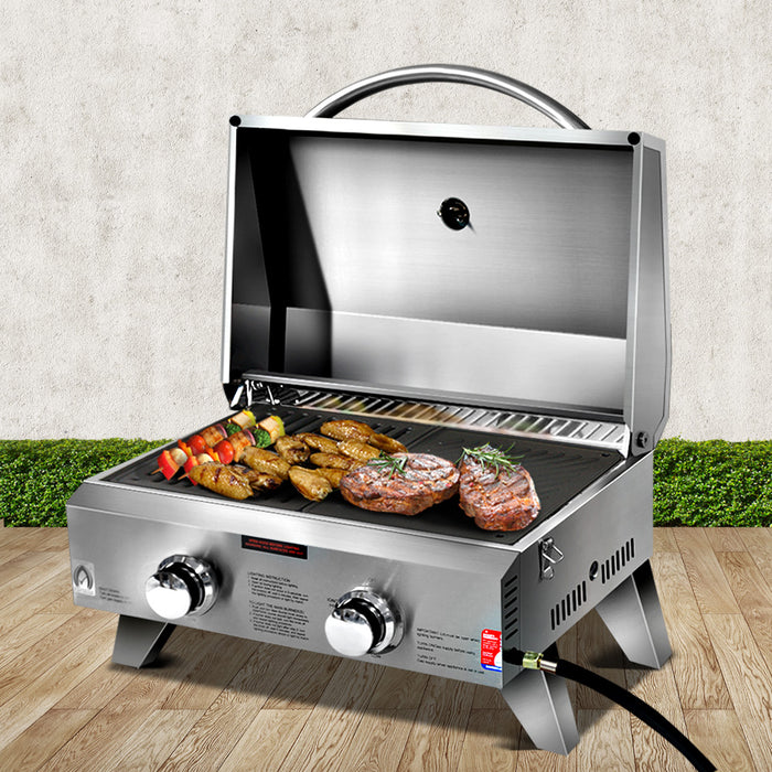Portable gas grill with food on a wooden surface and grass background