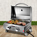 Portable gas grill with food on a wooden surface and grass background